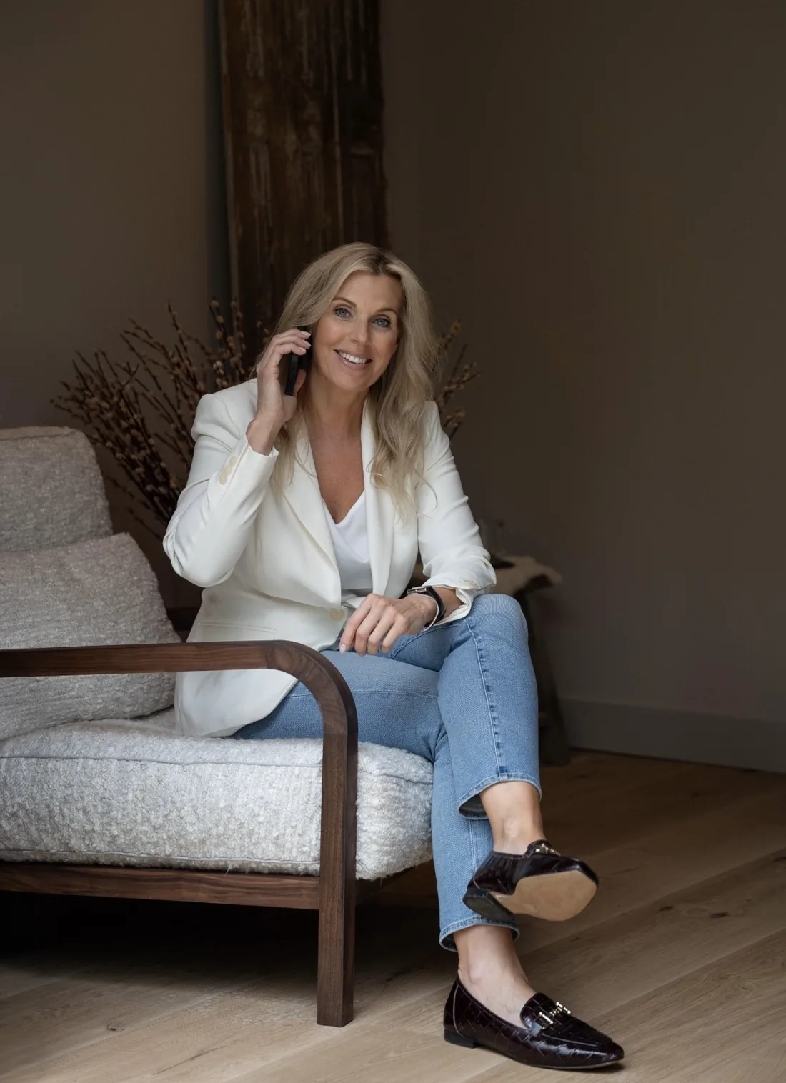 Angélique in een witte blazer, zittend in een fauteuil, aan de telefoon